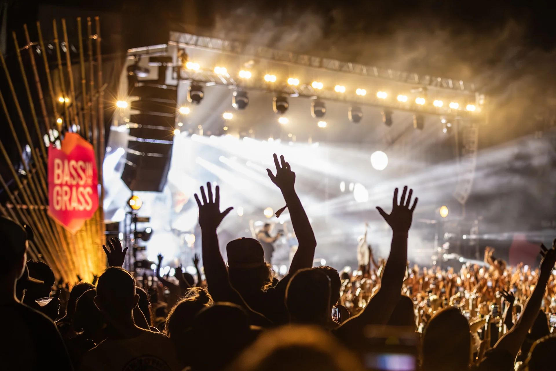 Concert crowd with their hands up in the air, stage lights in the background